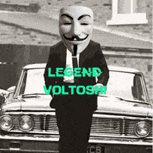 a man wearing an anonymous mask is standing in front of a car with legend voltoshi written on it