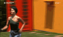 a woman in a black tank top is running in front of a red telephone booth on a tv screen