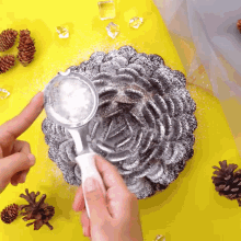 a person sprinkles powdered sugar on a cake on a yellow table