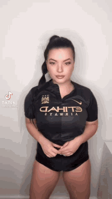 a woman wearing a black shirt that says ' manchester city ' on it is standing in front of a white wall .