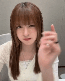 a young girl with long brown hair and bangs is sitting at a table making a funny face .