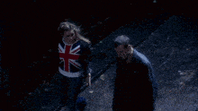 a woman wearing a british flag sweatshirt walks next to a man in a black jacket