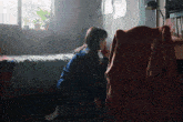 a woman sits on the floor in a bedroom with a sweater on the chair
