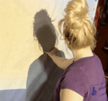 a woman in a purple shirt with the letter b on the back is touching her hair