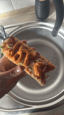 a person holding a slice of pizza with sauce on it in front of a sink