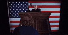 a man stands behind a podium with an american flag behind him