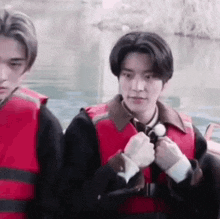 a man in a red life jacket is standing next to another man in a black jacket .