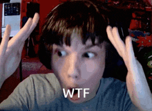 a boy wearing headphones has his hands on his head and the word wtf is on his face