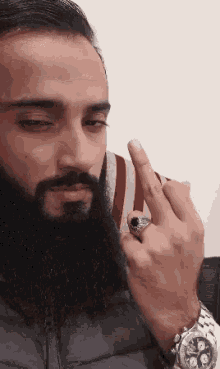 a man with a beard is wearing a watch and a ring on his finger