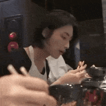 a man is sitting at a table eating food with chopsticks while looking at his phone .