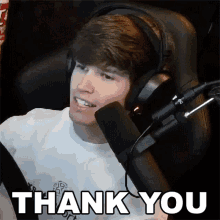 a young man wearing headphones is sitting in front of a microphone and saying thank you