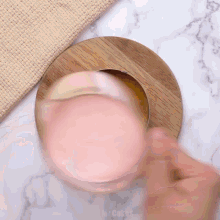 a person holding a glass of pink liquid on a wooden tray
