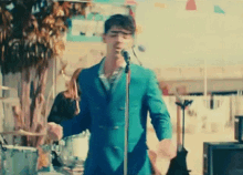 a man in a blue suit is singing into a microphone while a woman plays drums .