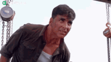 a man in a green shirt is standing next to a crane and looking at the camera .