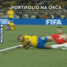 a soccer player is laying on the field while another player tries to tackle him .
