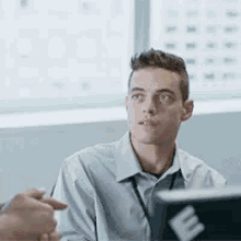 a man is sitting at a table in front of a laptop computer and looking at something .