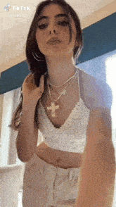 a woman wearing a crocheted crop top and a cross necklace is standing in front of a window .