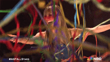 a woman in a blue dress is surrounded by colorful ribbons and a nbc logo