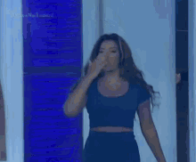 a woman in a blue dress is standing in front of a blue wall and waving .