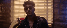 a man wearing sunglasses and a leather jacket is standing in front of a window