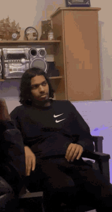 a man wearing a black nike sweatshirt sits on a chair