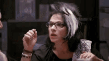 a woman with glasses and purple and white hair is sitting at a table .