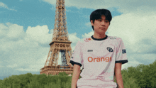 a man wearing an orange shirt stands in front of an eiffel tower