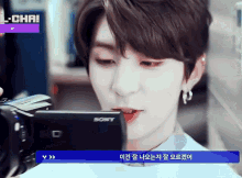 a young man looks at a sony camera with a purple l-chai sign in the corner