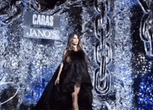 a woman in a long black dress is standing in front of a sign that says caras jano 's