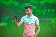 a man in a pink and blue shirt is taking a selfie with his phone