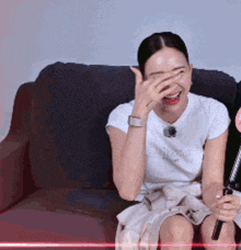a woman is sitting on a couch laughing and covering her face with her hand