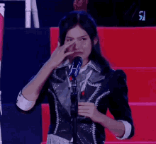 a woman is crying in front of a microphone with the letter r on the screen behind her