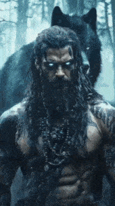 a man with long hair and a beard is standing next to a wolf with blue eyes