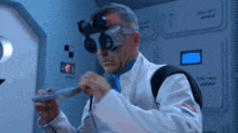 a man in a lab coat and goggles holds a small object in his hand