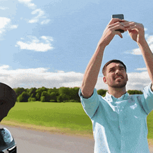 a man in a blue shirt is taking a picture of a field with his phone