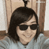 a woman wearing sunglasses and a sweater is smiling and taking a selfie .