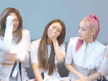 a girl with pink hair is covering her mouth while sitting next to two other girls