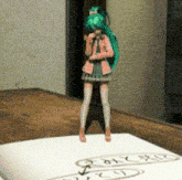 a figurine of a girl with green hair is standing on a piece of paper that says " i love you "