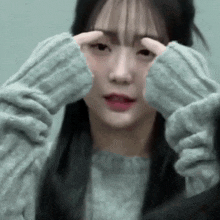 a close up of a woman wearing a sweater covering her eyes with her hands .