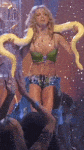 a woman in a green top and shorts is holding a yellow snake around her neck