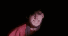 a man with a beard is crying in the dark while wearing a red sweater .