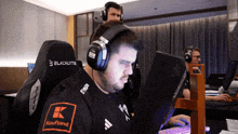 a man wearing headphones and a shirt that says kaufland sits in front of a computer