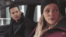a man and a woman are sitting in a car with uc written on the back of the jacket