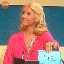 a woman in a pink shirt is holding a sign with the word tie written on it