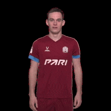 a soccer player in a maroon shirt and blue shorts is standing with his hands on his knees .
