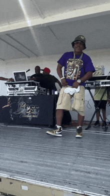 a man in a purple shirt stands on a stage in front of a boss entertainment table