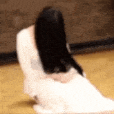 a woman in a white dress is sitting on the floor with her head in her hands .