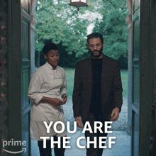 a man in a suit stands next to a woman in a chef 's uniform and says " you are the chef " in white
