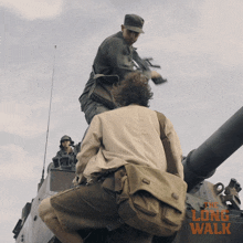 a man is riding on the back of a tank with a long walk advertisement behind him