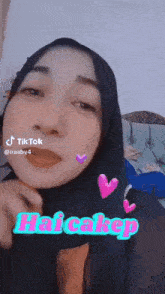 a woman wearing a hijab is making a funny face and has the word haicakep on her face .